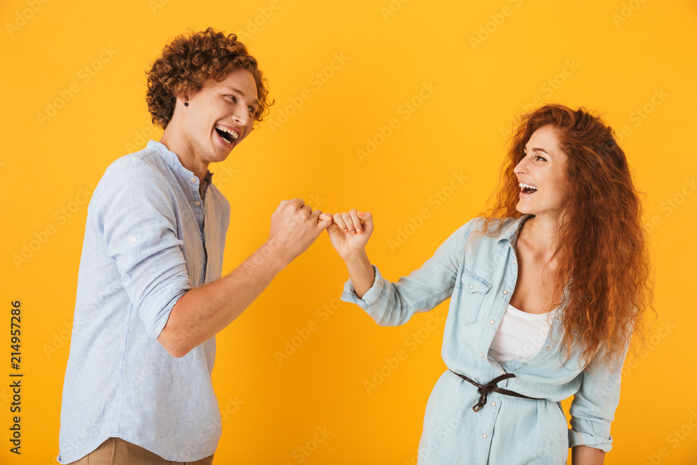 Photo of happy people man and woman smiling and hook each other's little fingers in conciliation or friendship, isolated over yellow background Photo of happy people man and woman smiling and hook each other's little fingers in conciliation or friendship, isolated over yellow background