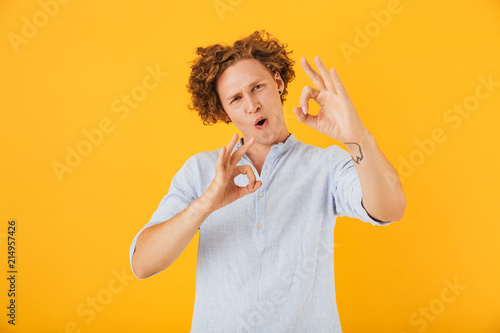 Photo of satisfied young guy 20s smiling and showing ok sign with fingers at camera  isolated over yellow background