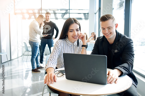 Beautiful young business couple are using a laptop, talking and smiling while working in office