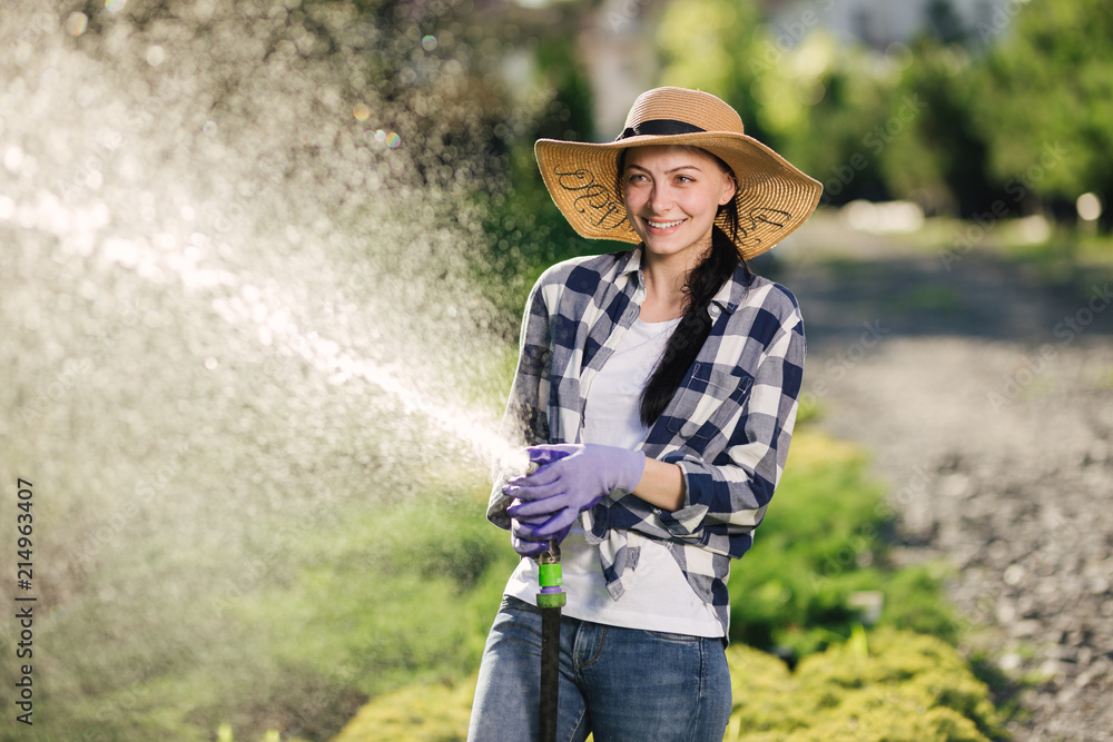 Beautiful young gardener woman having fun while watering garden in hot summer day