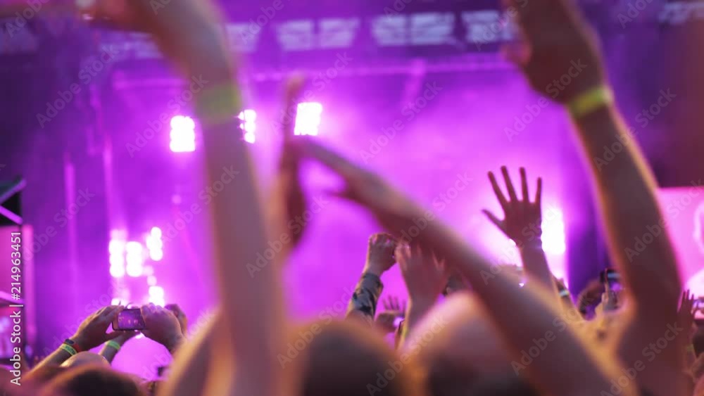 Slow motion shot of excited audience applauding, waving hands and shooting mobile videos at the concert, view against illuminated stage Slow motion shot of excited audience applauding, waving hands and shooting mobile videos at the concert, view against illuminated stage