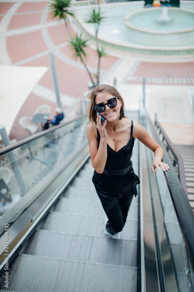 Young beauty woman speaks by phone on an escalator going down in city mall
