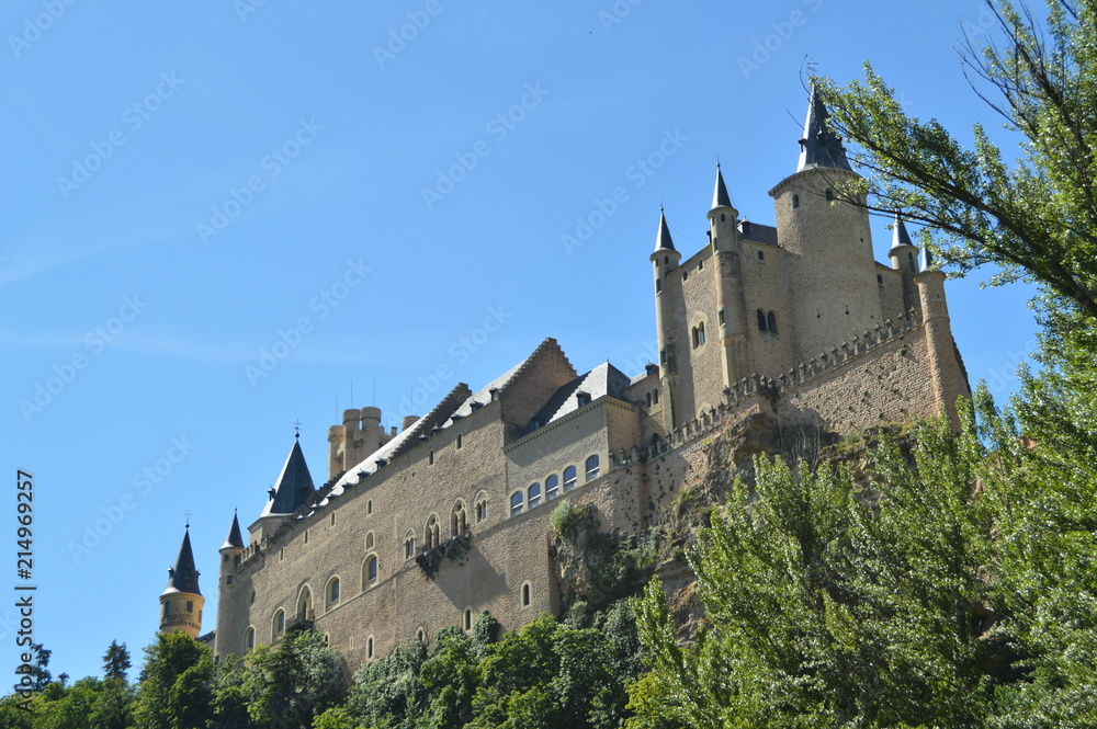 Alcazar Castle Seen From The River That Runs Through The Valley That Reigns In Segovia Slightly Caught By A Small Grove. Architecture, Travel, History. June 18, 2018. Segovia Castilla Leon Spain.