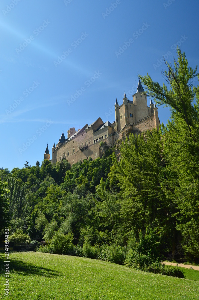 Alcazar Castle That Runs Through The Valley That Reigns In Segovia Slightly Caught By A Small Grove With Precious Beams Of Light In The Shot. Architecture, Travel, History. June 18, 2018. Spain.