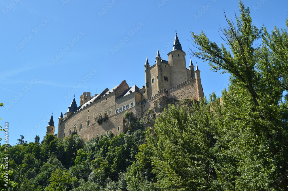 Alcazar Castle Seen From The River That Runs Through The Valley That Reigns In Segovia Slightly Caught By A Small Grove. Architecture, Travel, History. June 18, 2018. Segovia Castilla Leon Spain.