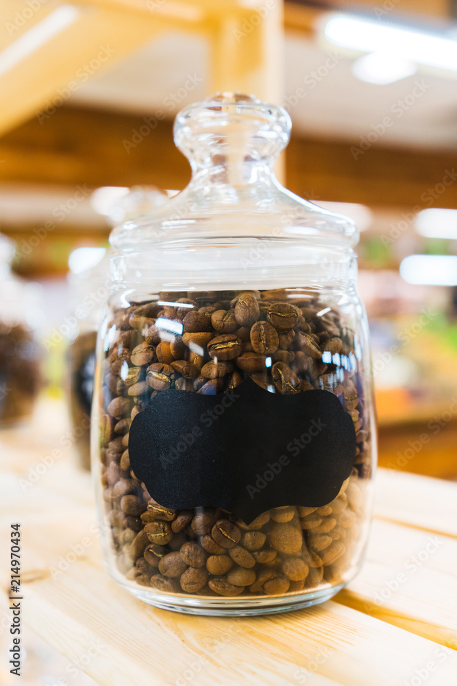 Traditional black coffee beans in a glass jar on the counter of a small market or store. 