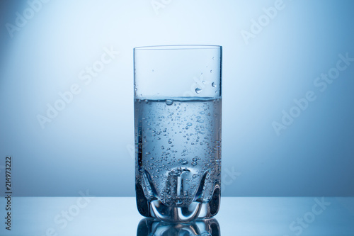 Glass of cold fresh sparkling mineral water on blue grandient background. photo