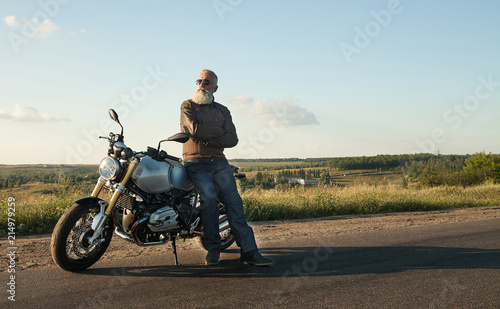 Biker man wearing a leather jacket and sunglasses sitting on his motorcycle.