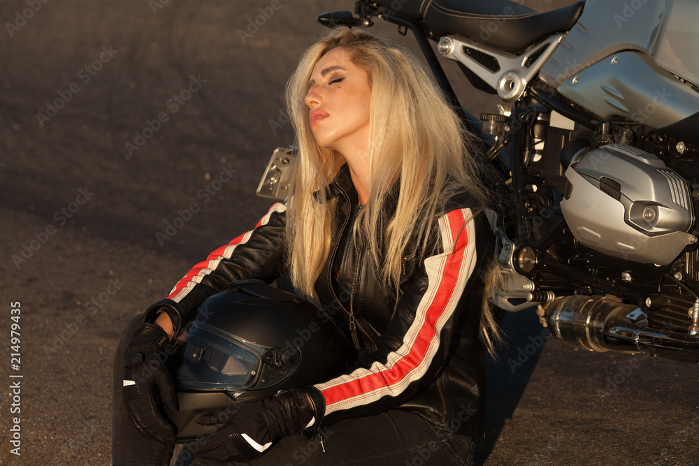Naklejka premium Beautiful biker woman sitting by her motorcycle on a highway. The spirit of freedom and independence.