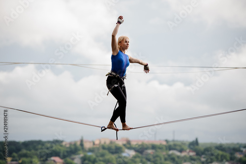 Young woman walking with one arm raised and other to the left on the slackline
