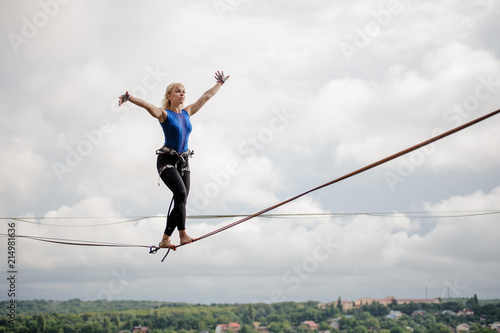 Obraz na płótnie Young smiling woman balancing with arms raised on the slackline rope