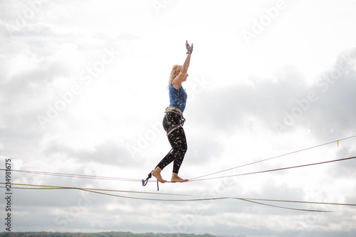 Side view young woman balancing on the slackline rope and looking into the distance