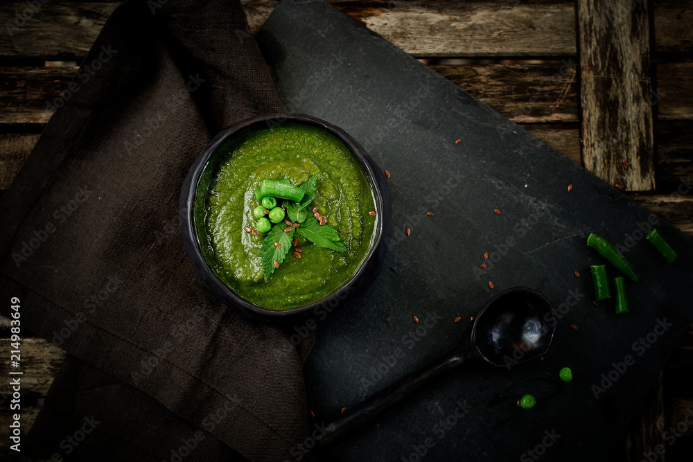 Green broccoli soup, on a gray stand, and a wooden background. Rustic style. Simple, nutritious vegetarian food. Decorated with seeds. With linen napkin Green broccoli soup, on a gray stand, and a wooden background. Rustic style. Simple, nutritious vegetarian food. Decorated with seeds. With linen napkin