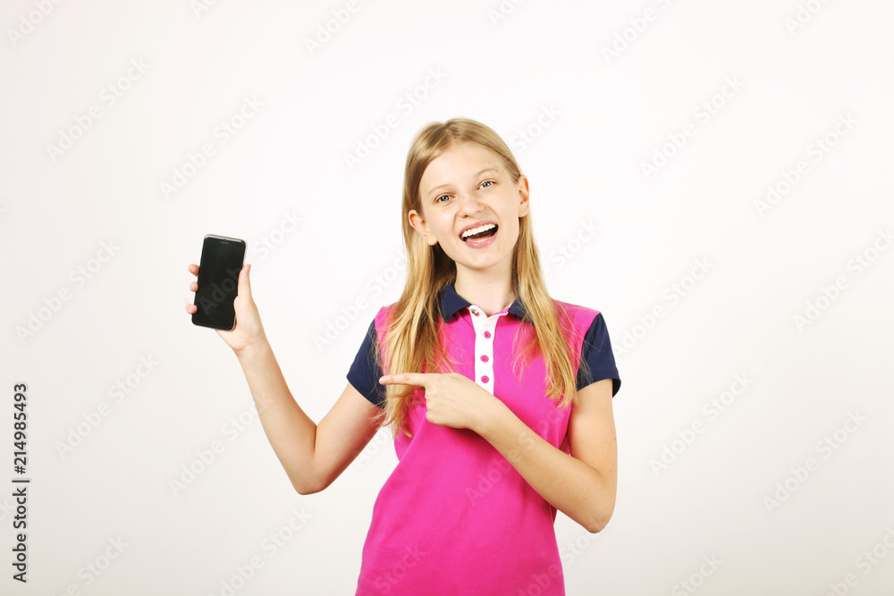 Portrait of casual teen age girl with long natural blond hair, index finger pointing at blank screen cell phone. Happy young female holding smartphone, showing display. White background, copy space Portrait of casual teen age girl with long natural blond hair, index finger pointing at blank screen cell phone. Happy young female holding smartphone, showing display. White background, copy space