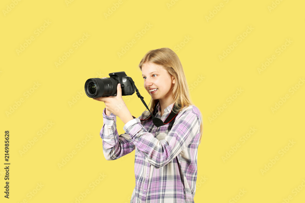 Young teenage girl holding digital photo camera with big lens & strap,  taking pictures, smiling. Beautiful blond female photographer in checkered  plaid shirt posing w/ dslr gear. Copy space background Photos