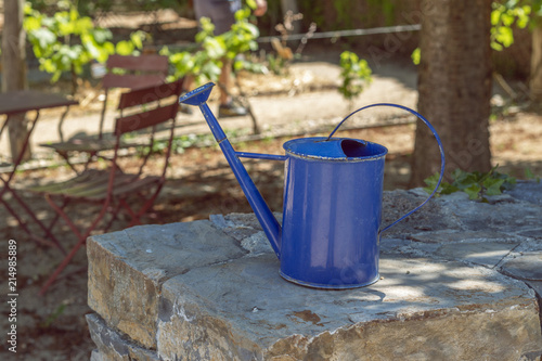 Blue watering can prepared to use in garden on dry sunny day