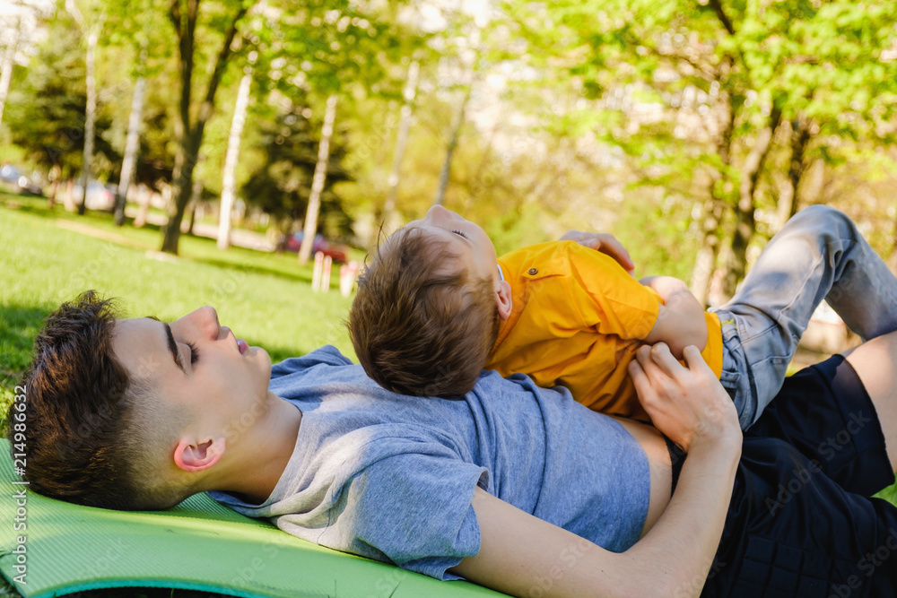 Cheerful two brothers lie on the grass in the park and play in funny games Cheerful two brothers lie on the grass in the park and play in funny games