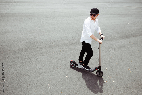 Modern man dressed white shirt and black pants standing at the street with electric scooter