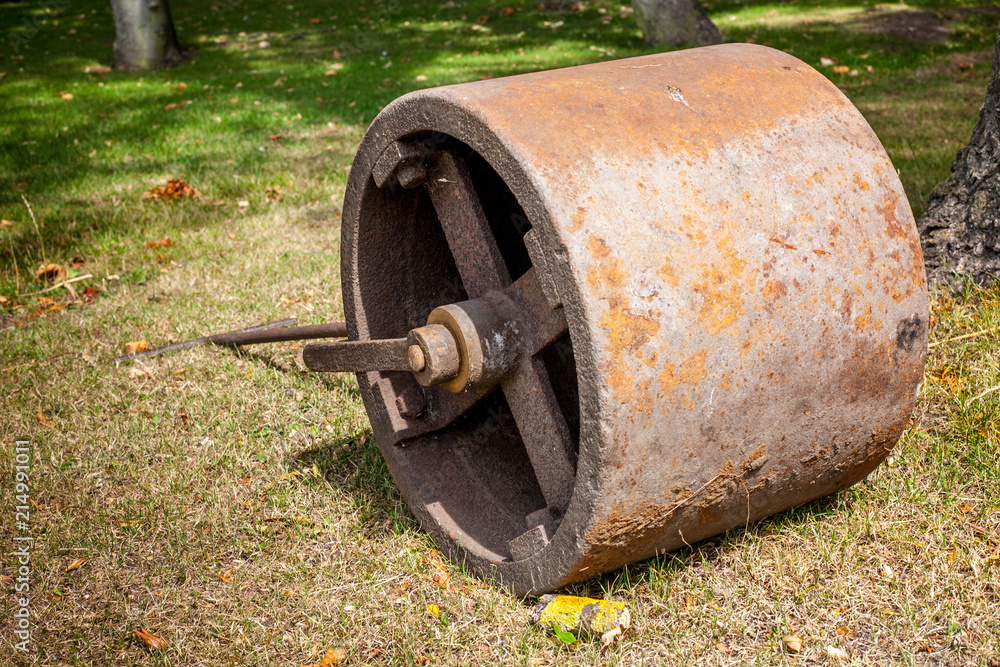 An old rusty metal lawn roller lying on some dried up grass