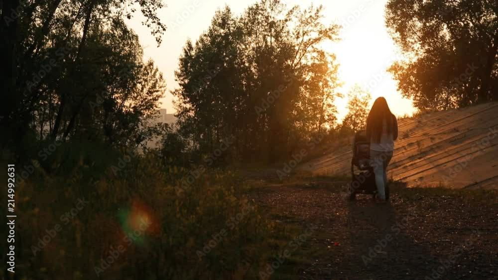 Young mother walks with a child sitting in a baby carriage at sunset. Young mother walks with a child sitting in a baby carriage at sunset.