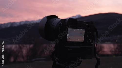 A man operating a mirrorless camera on a tripod during sunset in Queenstown, New Zealand photo