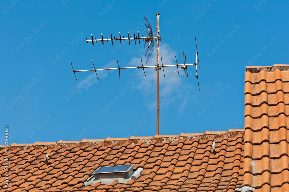 Eine alte Fernsehantenne auf einem Dach aus Tonziegeln unter blauem Himmel Eine alte Fernsehantenne auf einem Dach aus Tonziegeln unter blauem Himmel