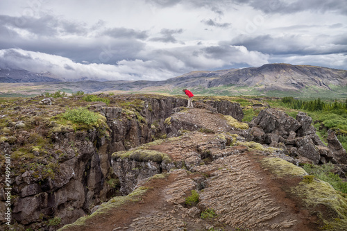 Woman standing on a cliff edge looking at rift valley, Thingvellir National Park, Iceland