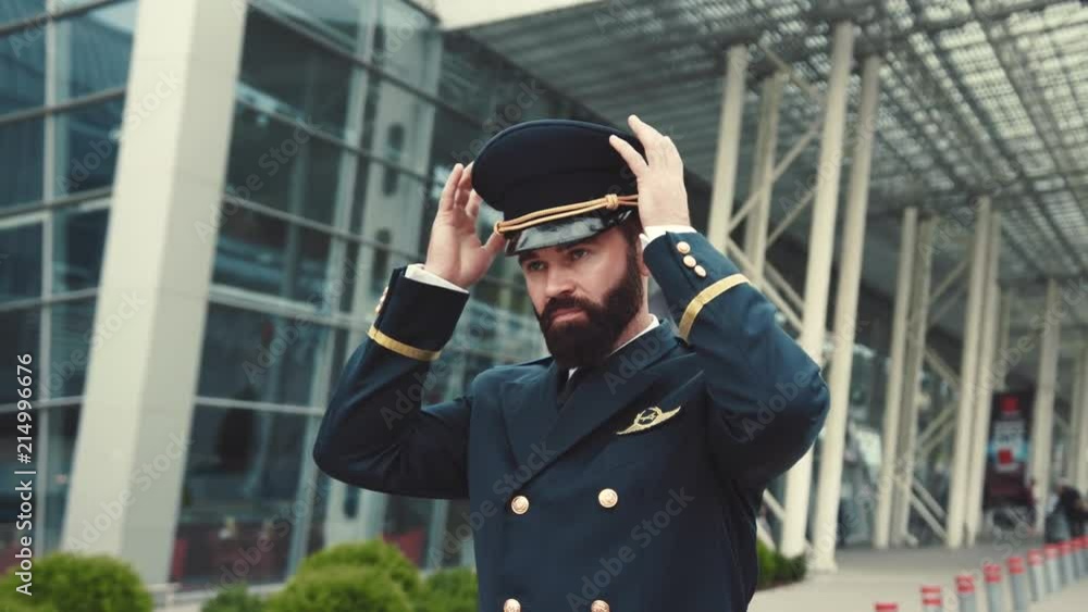 Stylish handsome bearded pilot puts on his pilot cap, corrects the uniform and confidently leaves the airport. Day off, weekend, profession concept. Male portrait Stylish handsome bearded pilot puts on his pilot cap, corrects the uniform and confidently leaves the airport. Day off, weekend, profession concept. Male portrait