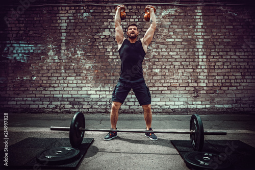 Athletic man working out with a kettlebell in front of brick wall. Strength and motivation. Outdoor workout. photo