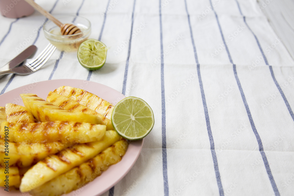 Grilled pineapple slices on a pink plate with honey and lime over striped napkin, low angle. Summer food. Closeup. Selective focus. Grilled pineapple slices on a pink plate with honey and lime over striped napkin, low angle. Summer food. Closeup. Selective focus.
