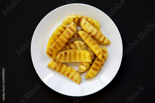 Top view, grilled pineapple wedges on a white plate over black background. Summer food. Closeup.