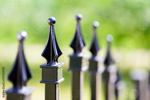 Black decorative metal fence, angular iron rods and curved upper part. Close-up of the top ornaments.