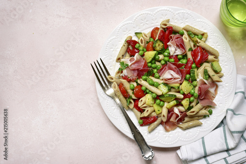Delicious whole wheat pasta penne with vegetables ( tomato, zucchini, grilled bell pepper, green pea ) and prosciutto.Top view with copy space.