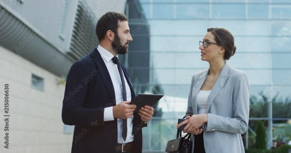 Attractive Caucasian woman in the business style standing at the big glass modern building and talking with handsome businessman. Attractive Caucasian woman in the business style standing at the big glass modern building and talking with handsome businessman.