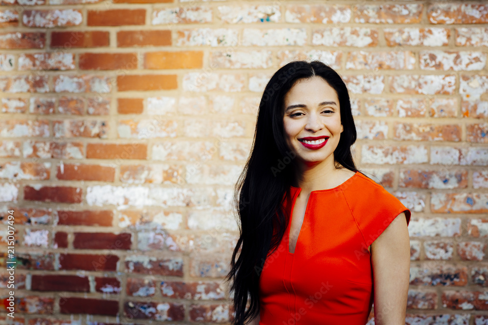 Smiling brunette in red dress in front of brick wall, looking off camera Smiling brunette in red dress in front of brick wall, looking off camera