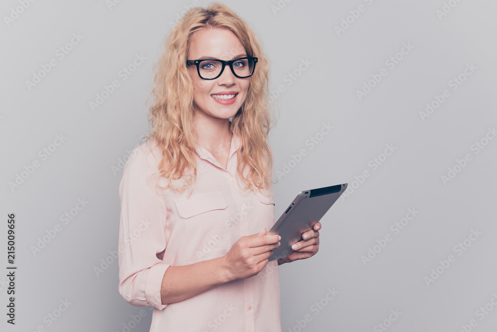 Portrait of clever smart attractive beautiful curly-haired cheerful blonde caucasian young girl wearing formal wear shirt and glasses, holding tablet. Isolated over grey background Portrait of clever smart attractive beautiful curly-haired cheerful blonde caucasian young girl wearing formal wear shirt and glasses, holding tablet. Isolated over grey background