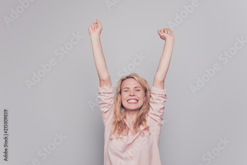 Wondered blond hair woman celebrates victory by raising her hands up isolated on gray background