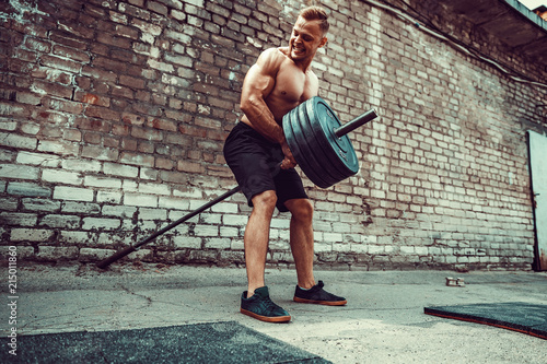 Athletic man working out with a barbell in front of brick wall. Strength and motivation. Outdoor workout. Exercise for the muscles of the back photo