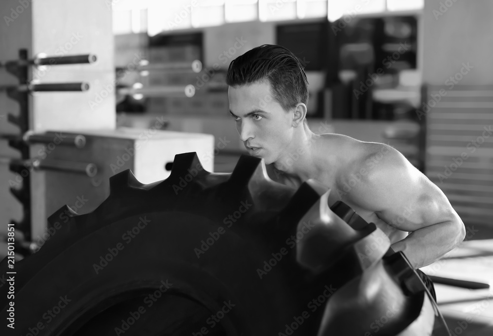 Young muscular man training with heavy tire in gym, black and white effect Young muscular man training with heavy tire in gym, black and white effect