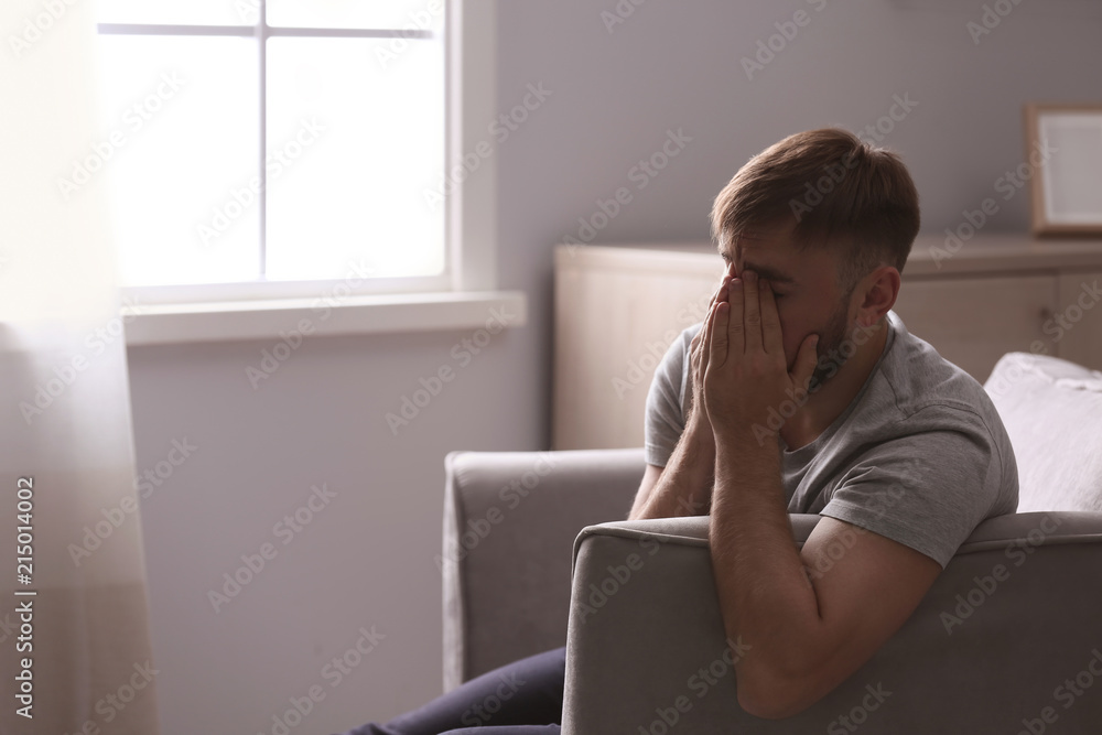 Depressed young man sitting in armchair at home Depressed young man sitting in armchair at home