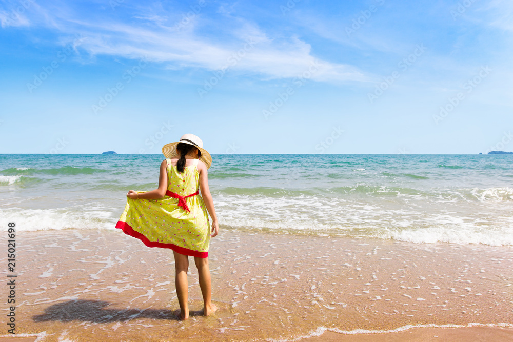 Little girl with yellow dress standing in water on the beach.Children girl relaxing and enjoying peace on vacation.Summer is coming and Summertime concept Little girl with yellow dress standing in water on the beach.Children girl relaxing and enjoying peace on vacation.Summer is coming and Summertime concept