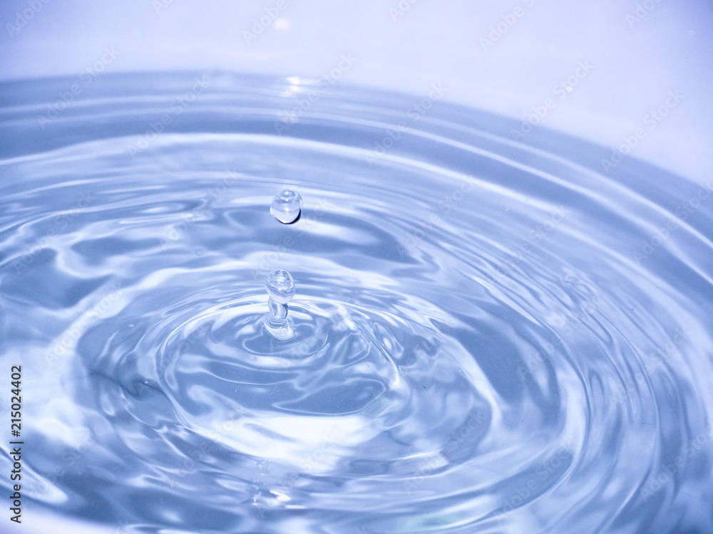 Close up blue water drop falling into water making a reflection concentric circles. Blue wave.