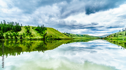 Fototapeta Naklejka Na Ścianę i Meble -  Dark Clouds and surrounding Mountains reflecting on the smooth water surface of Trapp Lake, located along Highway 5A between Kamloops and Merritt in British Columbia, Canada