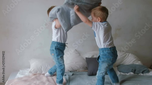 Twin boys toddlers are lying on the bed, throwing pillows, jumping and laughing.