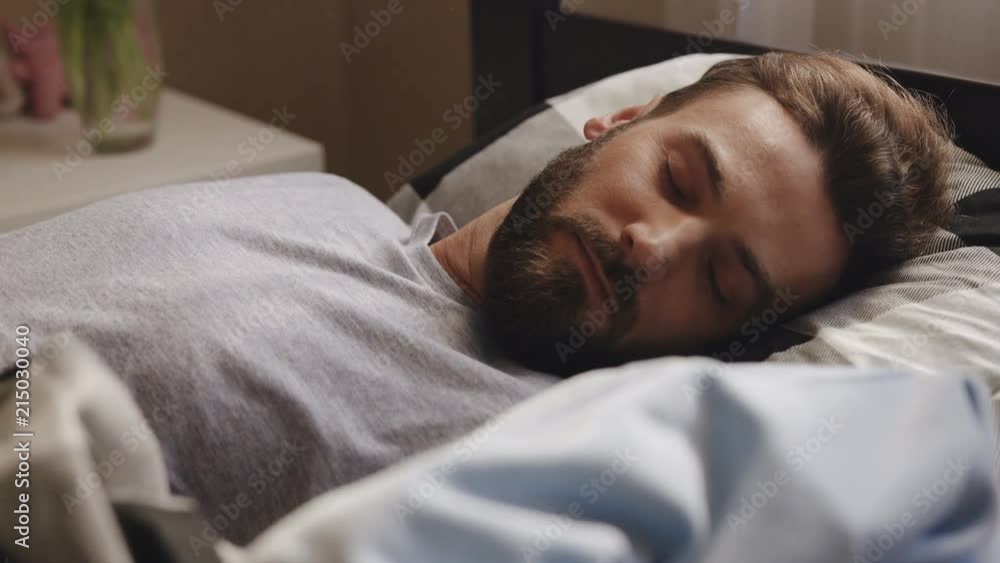 Close up of the handsome man with a beard lying and sleeping in the bed at home. Portrait shot. Indoor Close up of the handsome man with a beard lying and sleeping in the bed at home. Portrait shot. Indoor