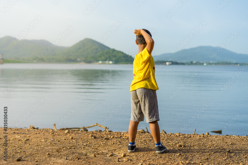 young boy throw stone into the water at Bang Pra Reservoir in sunset