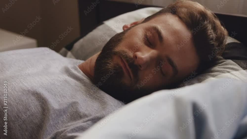 Close up of the man with a beard lying and sleeping in the bed at home. Portrait shot. Indoors Close up of the man with a beard lying and sleeping in the bed at home. Portrait shot. Indoors
