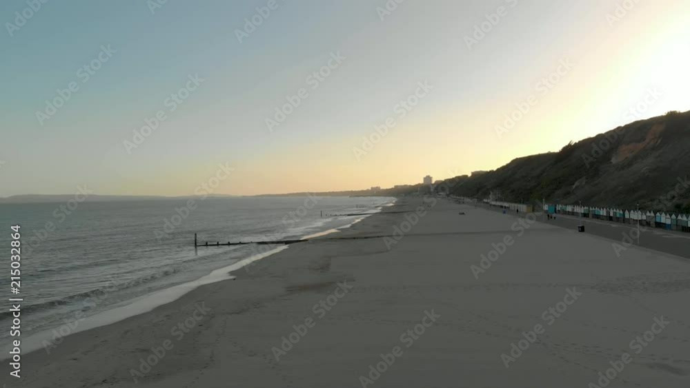 Aerial view of an English sandy beach strip, sea with waves, hill with houses and cabins, in a lateral movement towards the sea. Aerial view of an English sandy beach strip, sea with waves, hill with houses and cabins, in a lateral movement towards the sea.