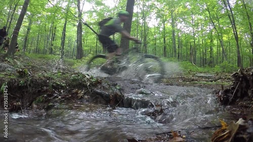 Low angle speed ramping shot of rushing stream as mountain bikers splash across it. photo