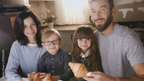 Close up of the nice smiled family sitting at the table with croissants and posing to the camera. Portrait shot. Indoors photo